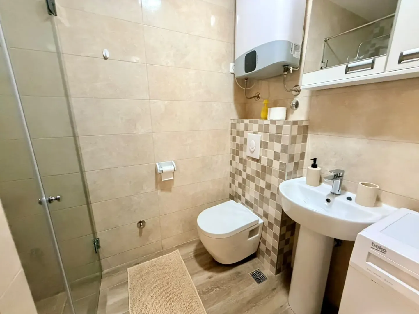 Manje kupatilo sa tuš kabinom, WC šoljom, umivaonikom i bojlerom.
