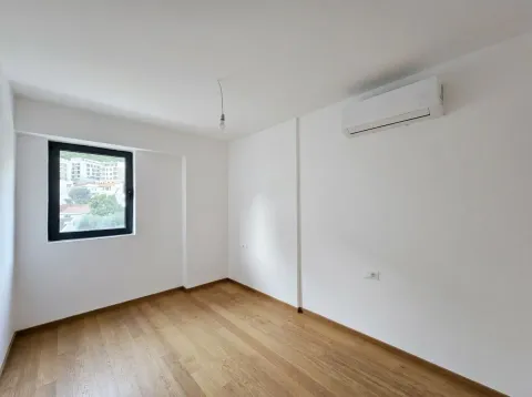 Prazna soba sa drvenim podom, klima uređajem i prozorom koji gleda na grad. - image 8