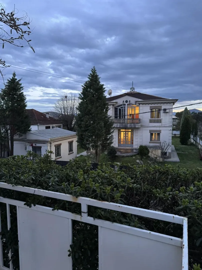 Pogled sa terase na dvospratnu kuću sa osvijetljenim prozorima u sumrak.