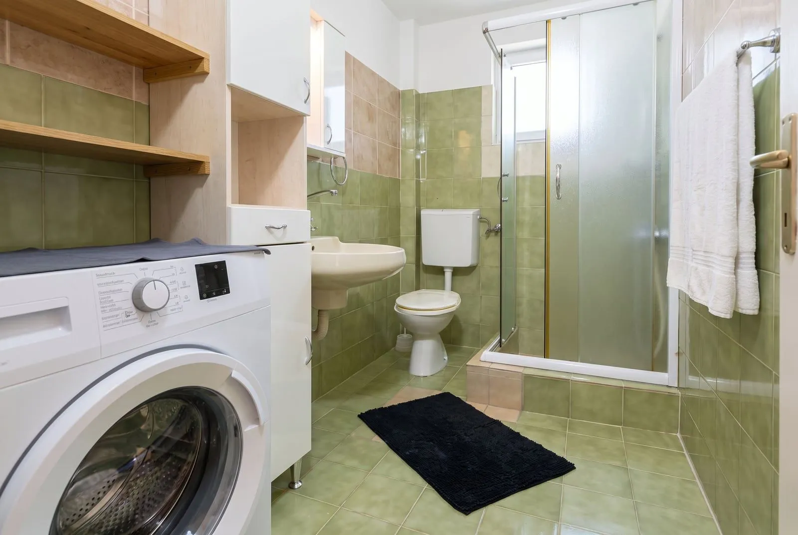 Small bathroom with a shower cabin, sink, toilet, and washing machine.