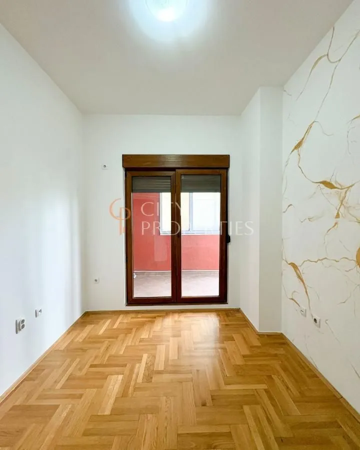 Empty room with hardwood flooring and balcony doors.