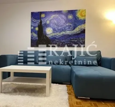 Dnevna soba sa plavom ugaonom garniturom, belim stočićem i slikom na zidu. - image 3