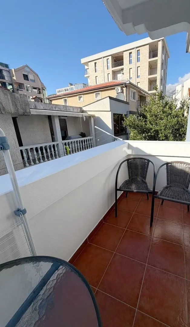 Manji balkon sa keramičkim pločicama, stolicama i pogledom na okolne zgrade.