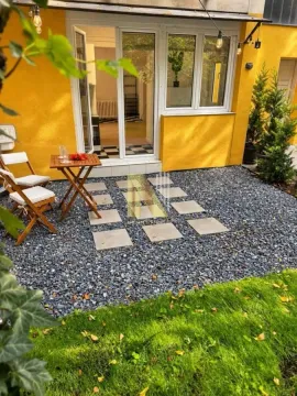 Uređeno dvorište sa popločanim stazama i malim stolom za sedenje ispred ulaza. - image 4