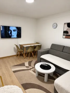 Dnevna soba sa sivom garniturom, stočićem, trpezarijskim stolom i zidnim televizorom. - image 2