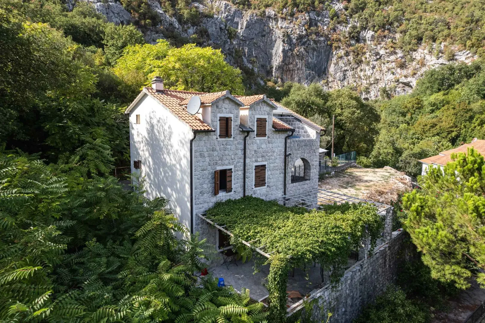 Pogled iz vazduha na kamenu kuću sa dvorištem i okruženjem u prirodi.