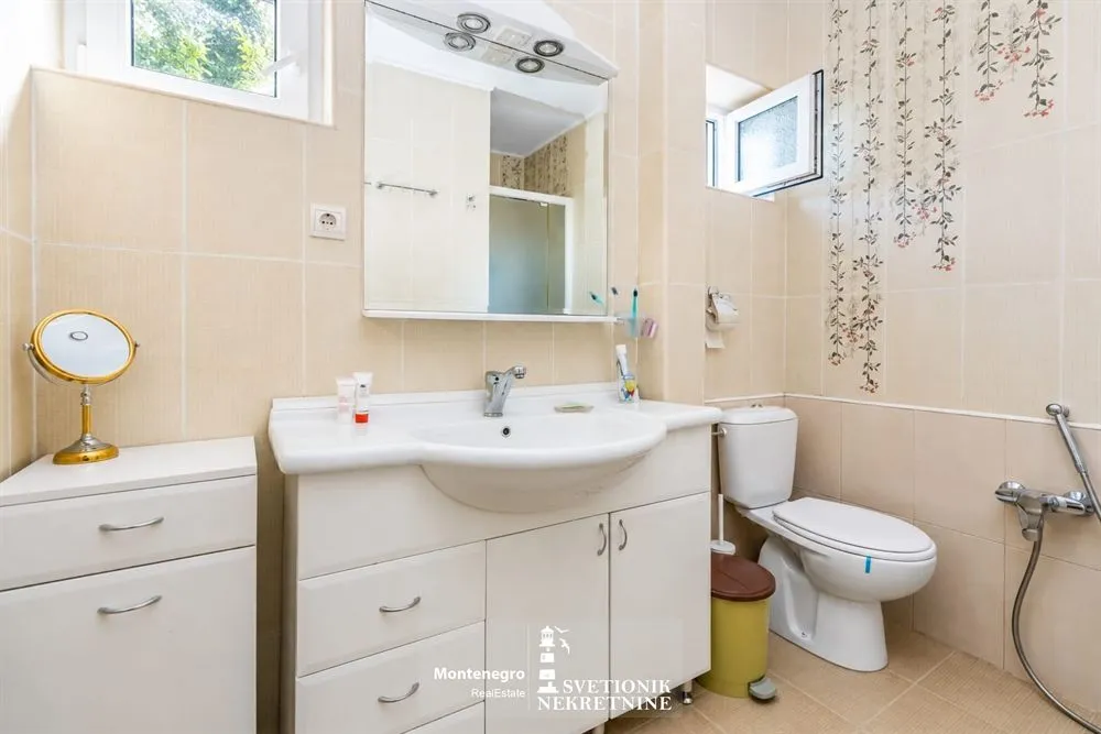 Svijetlo kupatilo sa umivaonikom, ogledalom i WC šoljom u bež tonovima.
