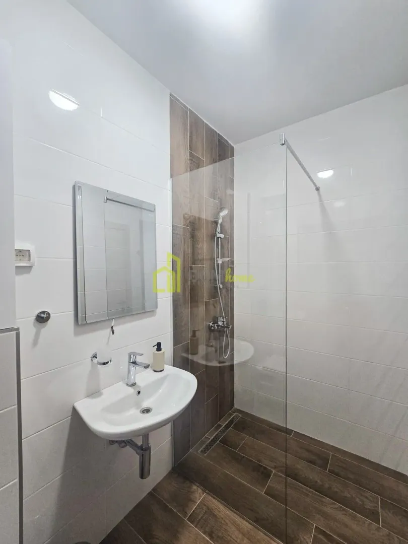 Moderne kupatilo sa umivaonikom, ogledalom i tuš kabinom sa staklenom pregradom.