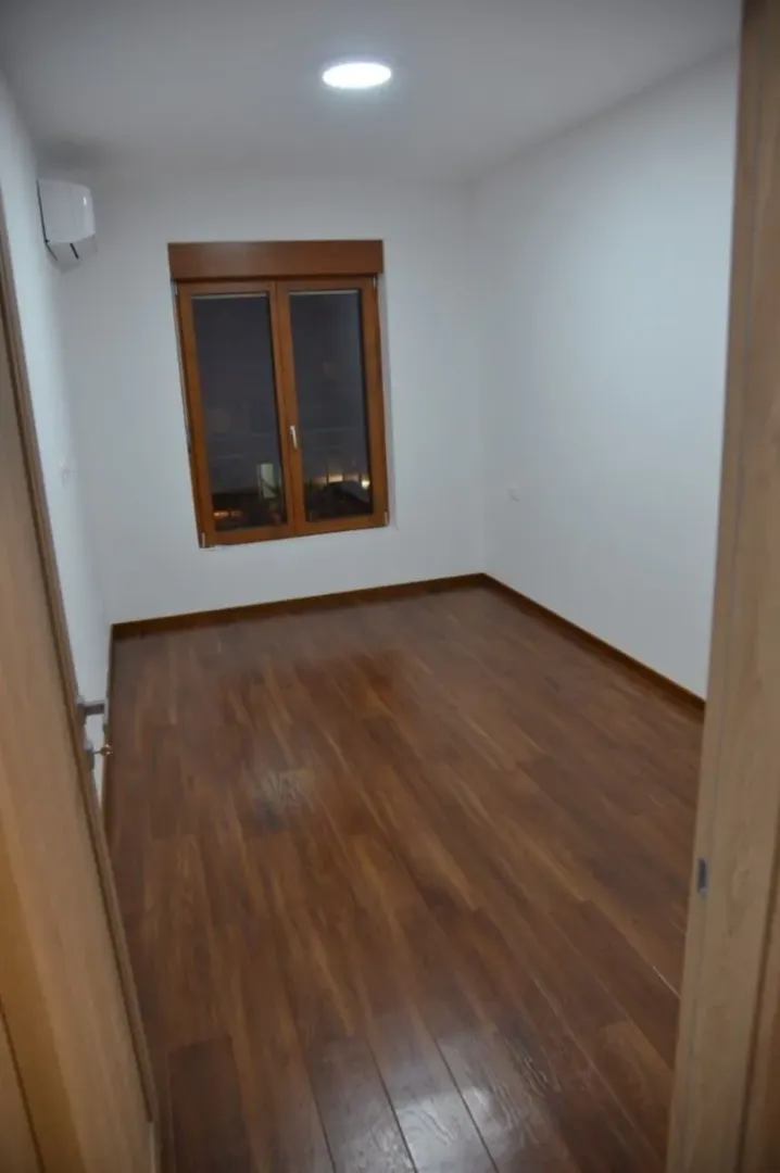 An empty room with light walls, wooden floor, and a window.