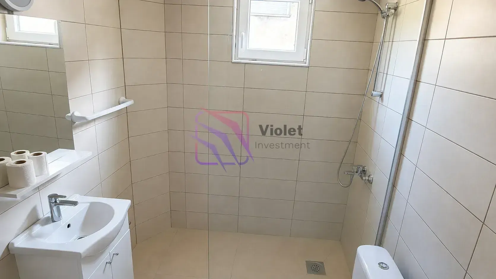 Kupatilo opremljeno umivaonikom, tuš kabinom sa staklenom pregradom i toaletom.