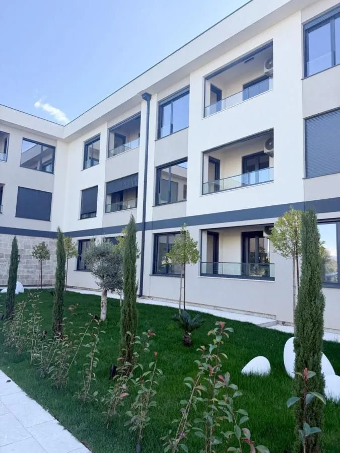 Pogled na fasadu zgrade sa uređenim dvorištem i zelenilom.