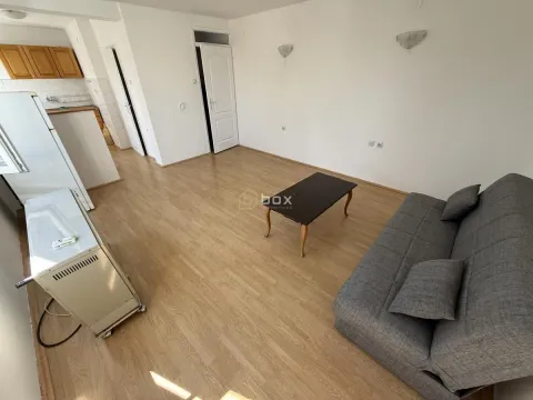 Dnevna soba sa sivom sofom, stočićem i delom kuhinje u pozadini. - image 4