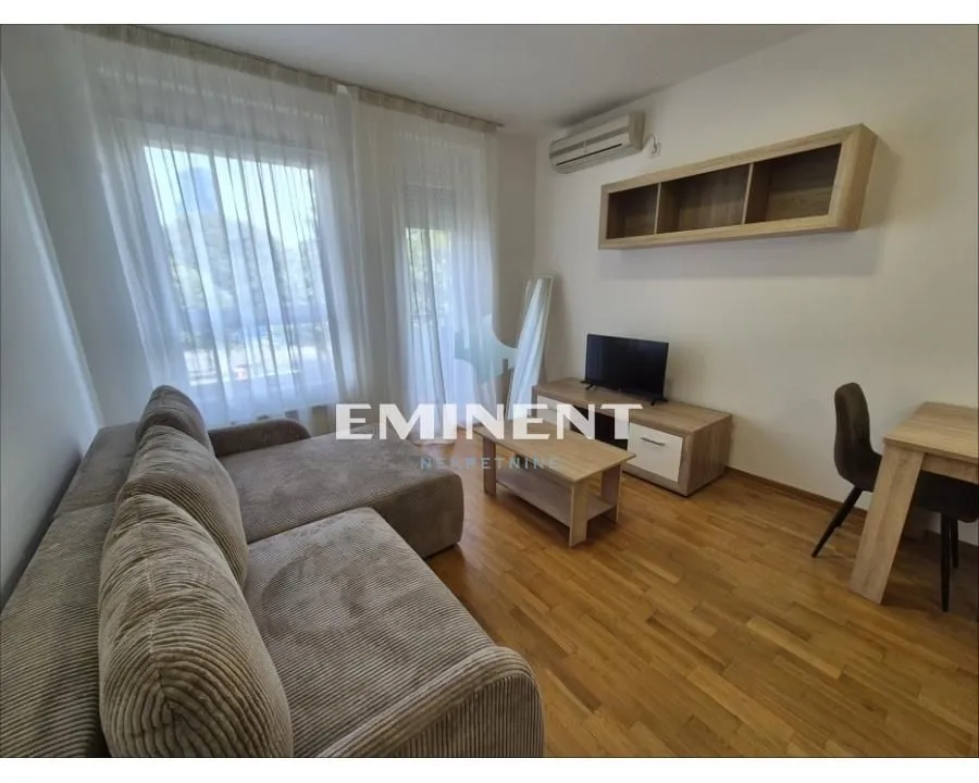 Nameštena dnevna soba sa garniturom, televizorom i trpezarijskim stolom.