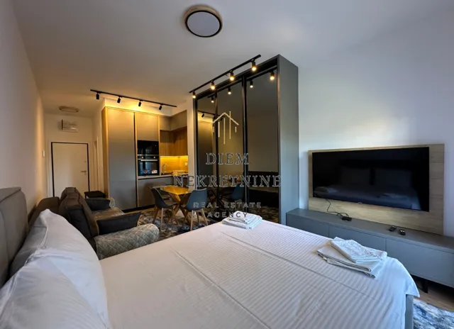 Spacious bedroom with a double bed, TV, and kitchen in the background.