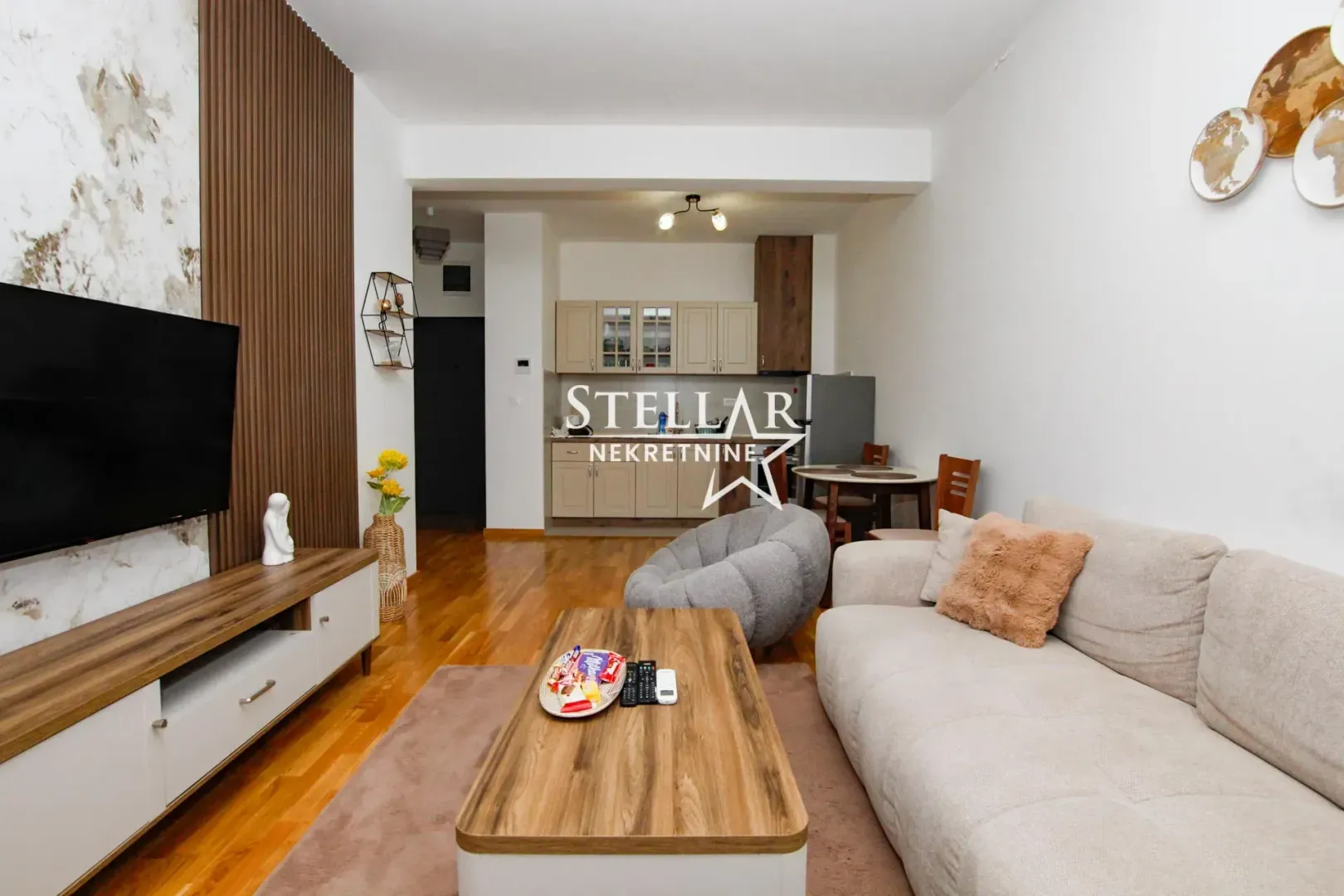 Living room with sofa, TV unit, and kitchen in the background.