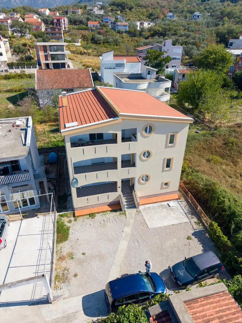 Aerial view of a multi-family house with a yard and parked cars.