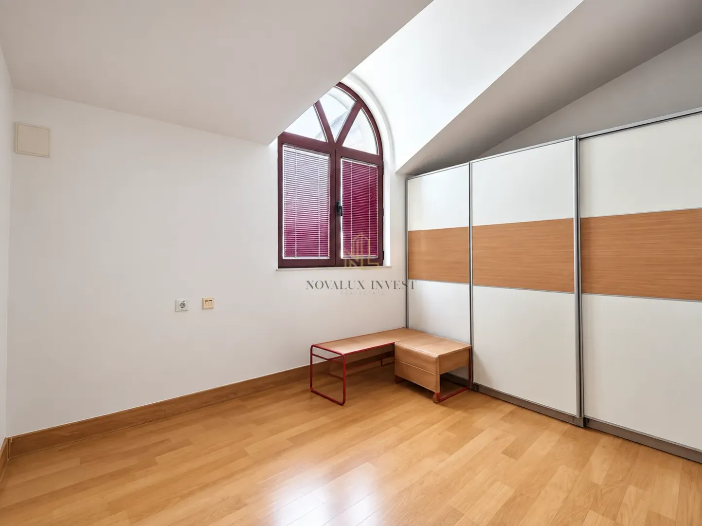 Attic room with a large arched window, wooden flooring, and a built-in wardrobe.