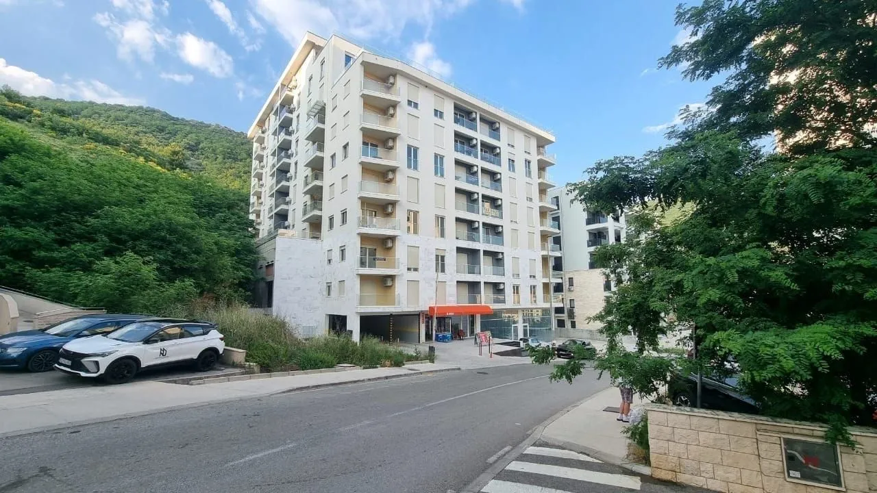 Eksterijer moderne stambene zgrade sa okolnim zelenilom i ulicom u prvom planu.