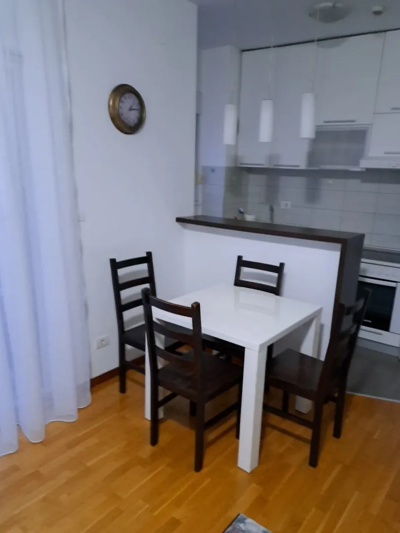 Trpezarijski sto sa stolicama i kuhinja u pozadini.