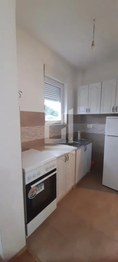 Manja kuhinja sa bijelim elementima, šporetom i frižiderom.