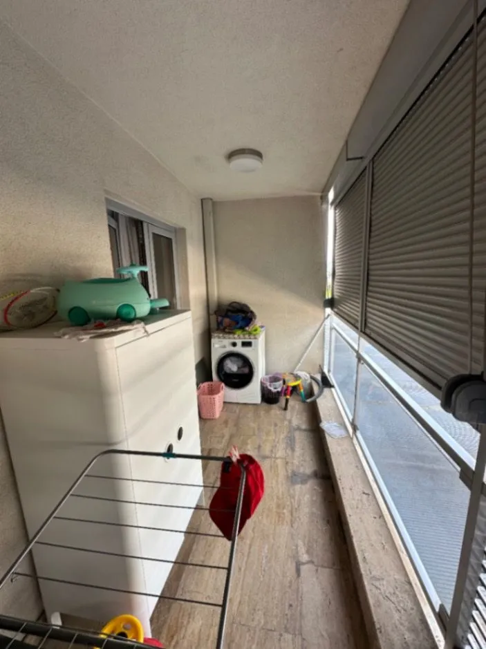 Covered terrace with a washing machine and a drying rack.