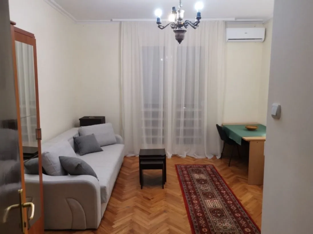 A simply furnished living room featuring a grey sofa and parquet flooring.