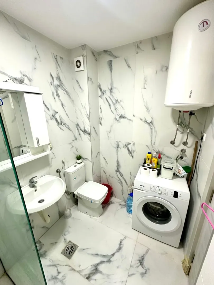Small bathroom with a shower enclosure, sink, toilet, and washing machine.
