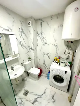 Small bathroom with a shower enclosure, sink, toilet, and washing machine. - image 3