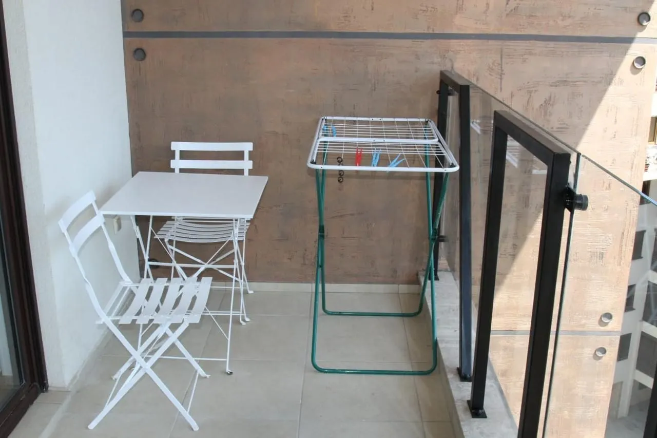 Small balcony with a white table, chairs, and a clothes drying rack.