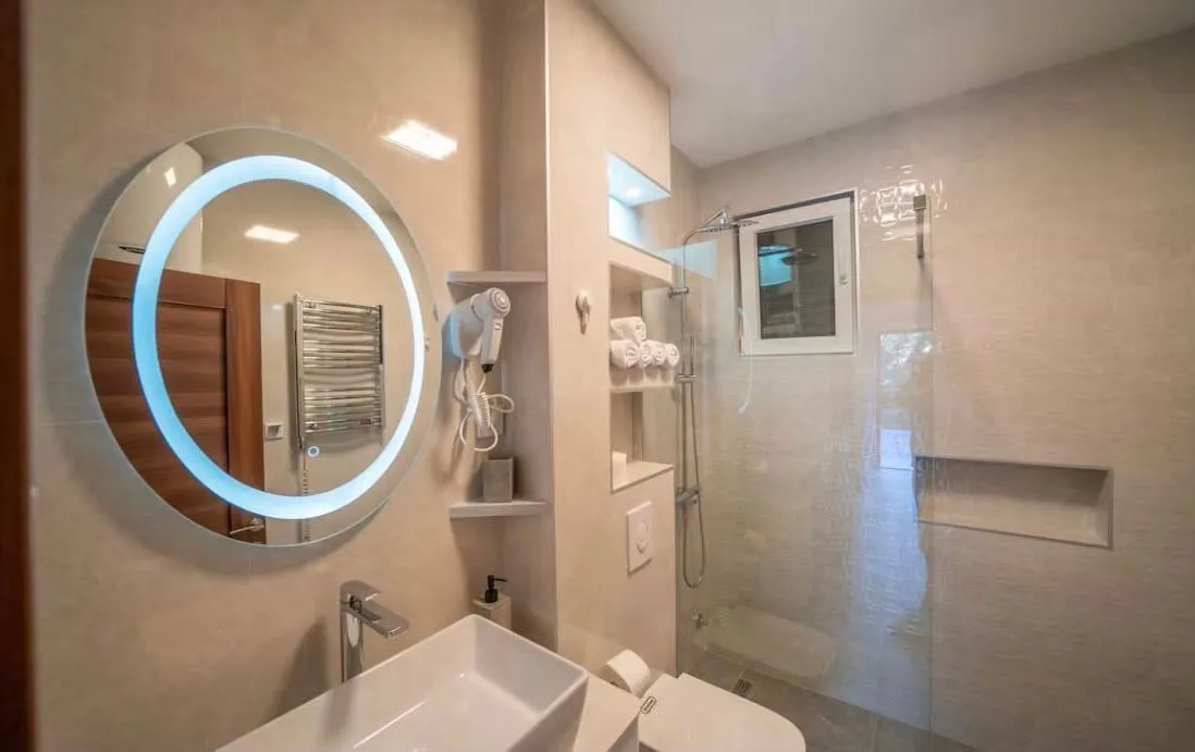Modern bathroom with an illuminated round mirror and a walk-in shower.