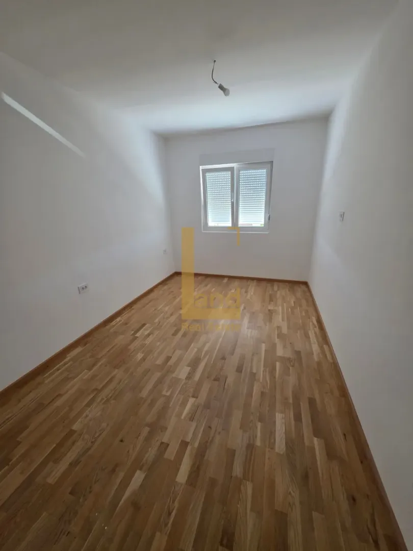Prazna soba sa parketom i bijelim zidovima.