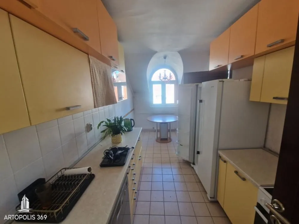 Dugačka kuhinja sa žutim elementima i trpezarijskim stolom kod prozora.