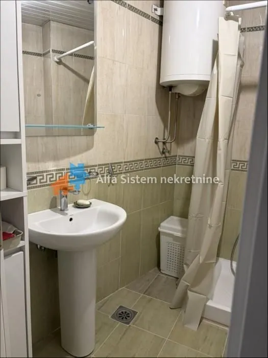 Manje kupatilo sa umivaonikom, ogledalom i tuš kabinom sa zavesom.