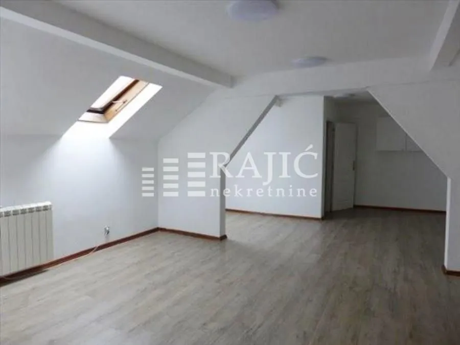 Empty attic room with laminate flooring and a skylight.