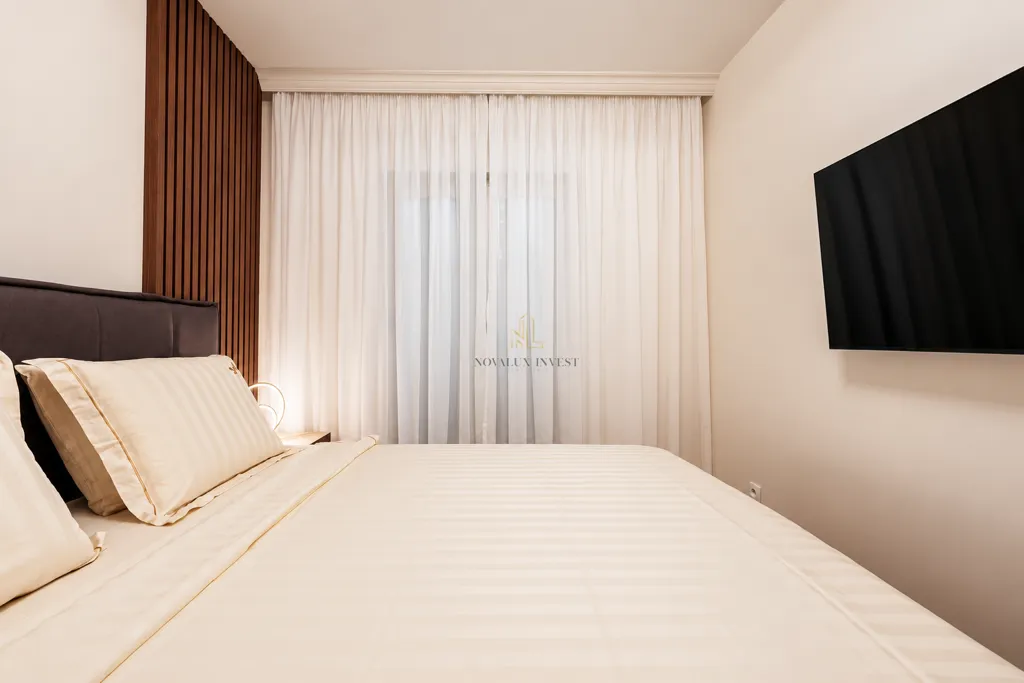 Modern bedroom with a double bed, white curtains and a wall-mounted TV.