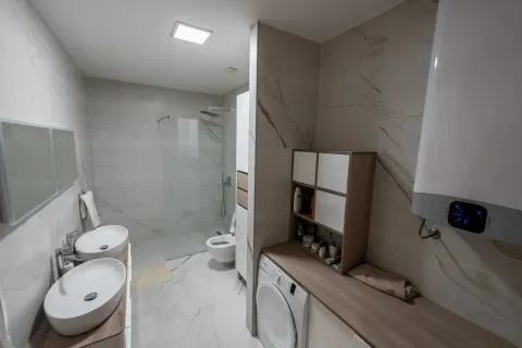 Modern bathroom with two washbasins, walk-in shower, and built-in washing machine. - image 8