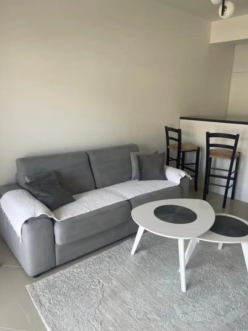 Bright living room with a grey sofa, white coffee table, and bar stools.