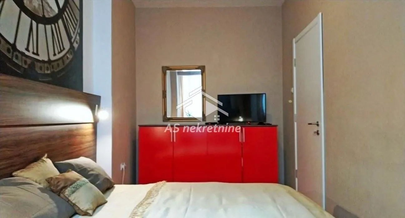 Furnished bedroom with a double bed, red dresser, and TV.