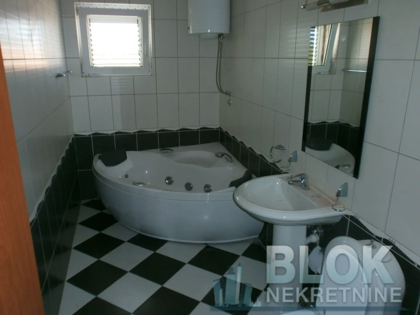 Bathroom equipped with a corner bathtub, washbasin, and black-and-white patterned tiles.
