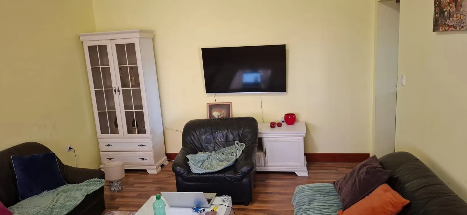 Dnevna soba sa garniturom za sjedenje, televizorom i bijelim namještajem.