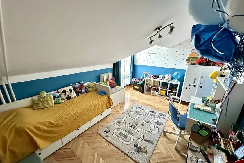 Dečja soba sa krevetom, radnim stolom i kosim plafonom.