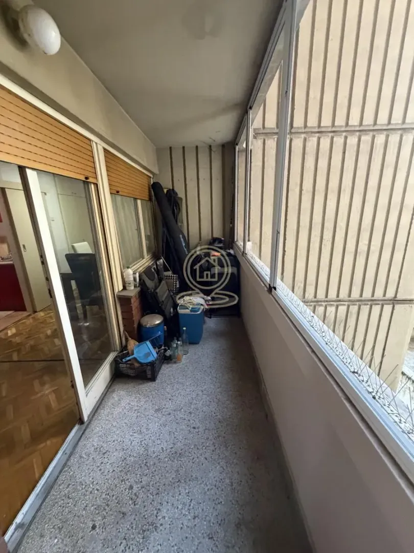 Zastakljeni balkon sa betonskim podom i raznim predmetima.