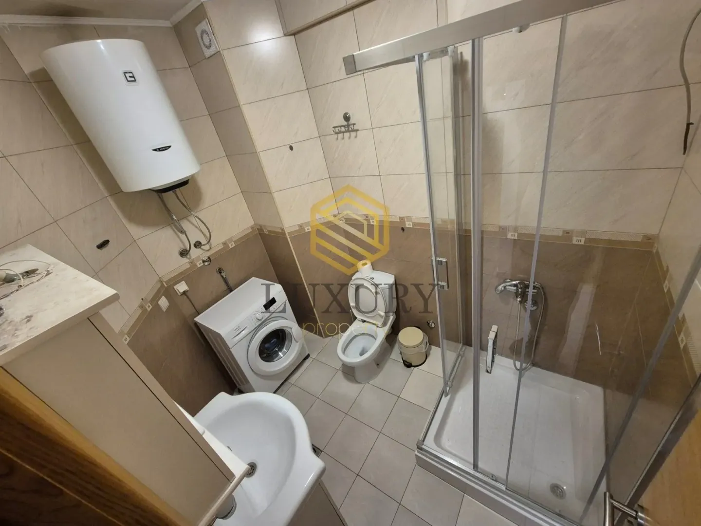 Smaller bathroom with a shower cabin, sink, washing machine, and water heater.