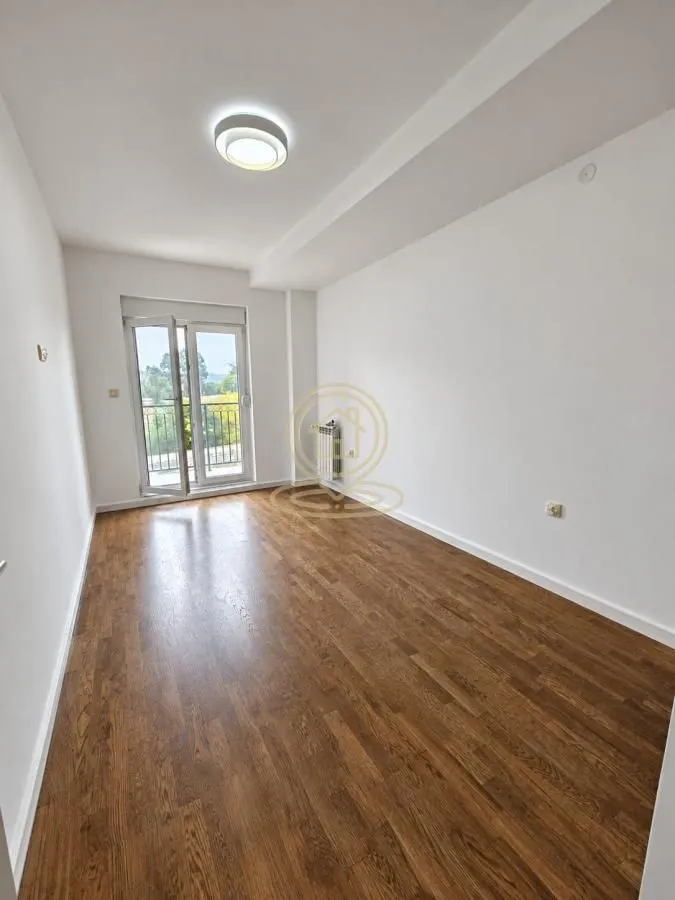 Empty room with wooden flooring and balcony doors.