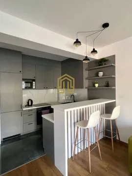 Moderna kuhinja sa šankom, trpezarijskim stolicama i sivim elementima. - image 9