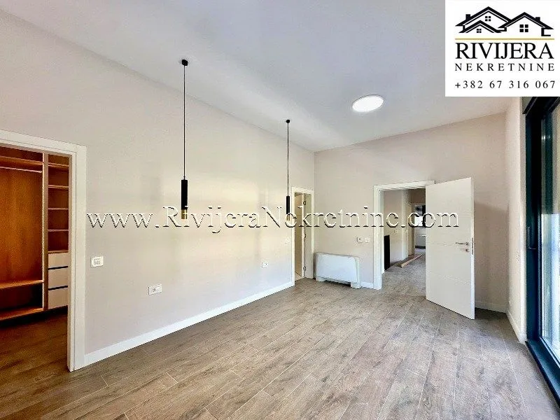 Spacious empty room with wooden flooring, pendant lights, and a walk-in closet entrance.