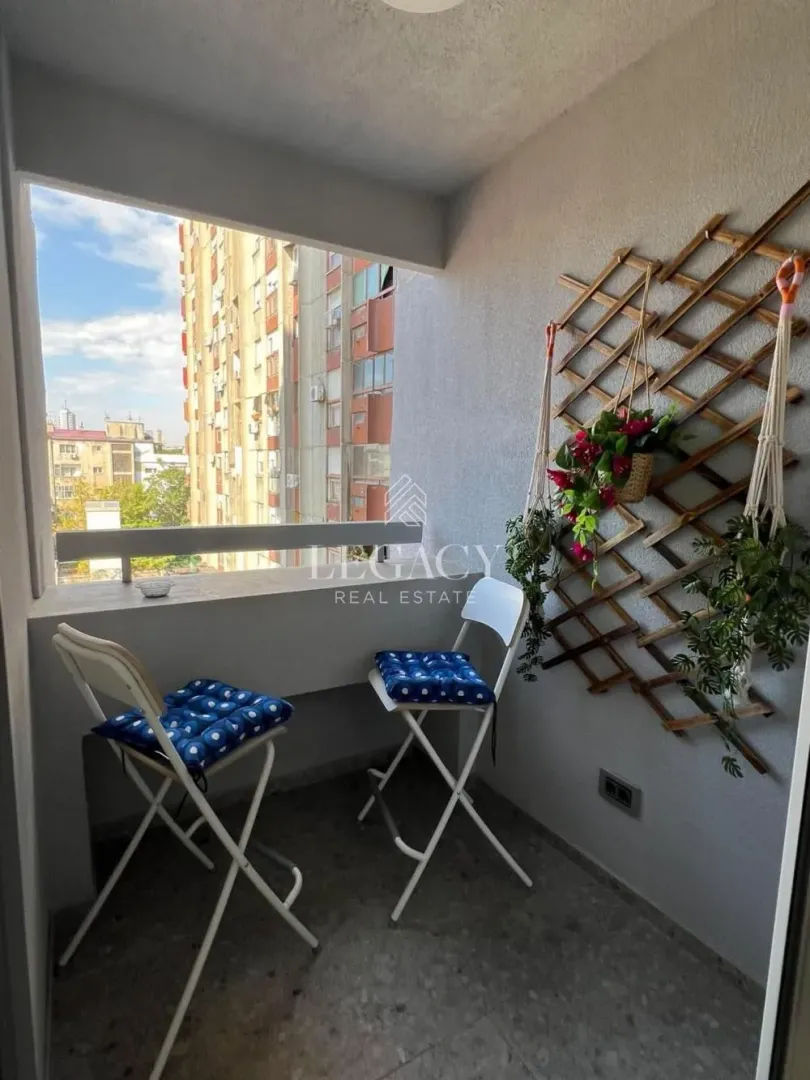 Smaller enclosed balcony with a glass railing, two chairs, and a decorative wall panel with plants.