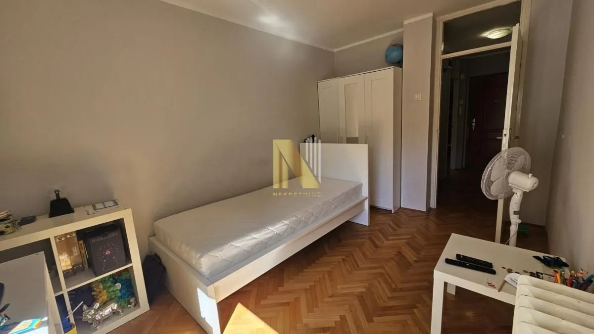 Manja spavaća soba sa krevetom, ormanom i drvenim podom.