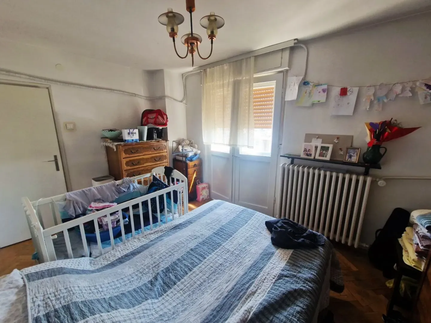 Spavaća soba sa bračnim krevetom, krevetcem za bebe i nameštajem.
