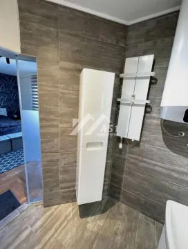 Pogled na kupatilo sa keramičkim pločicama u imitaciji drveta i belim ormarićem. - image 7